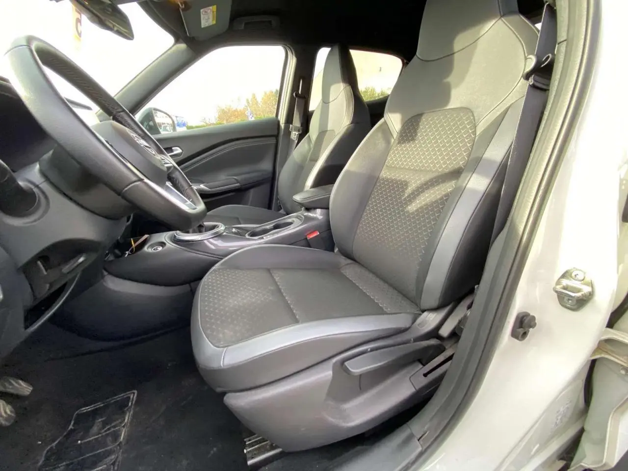 Vue intérieure côté conducteur du Nissan Juke blanc perle 2024, sièges noirs avec motifs géométriques et volant visible.