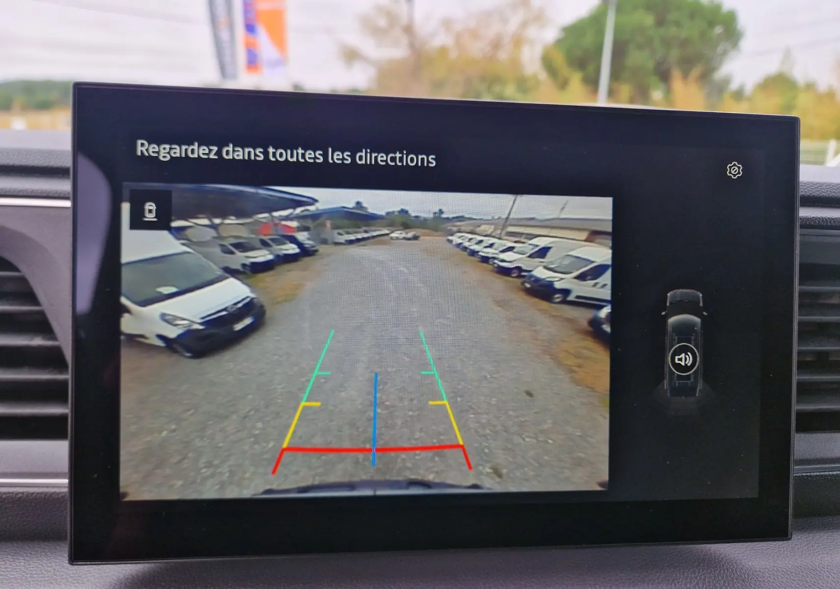 Écran de caméra de recul du Renault Master gris urbain montrant une allée avec plusieurs véhicules blancs stationnés.