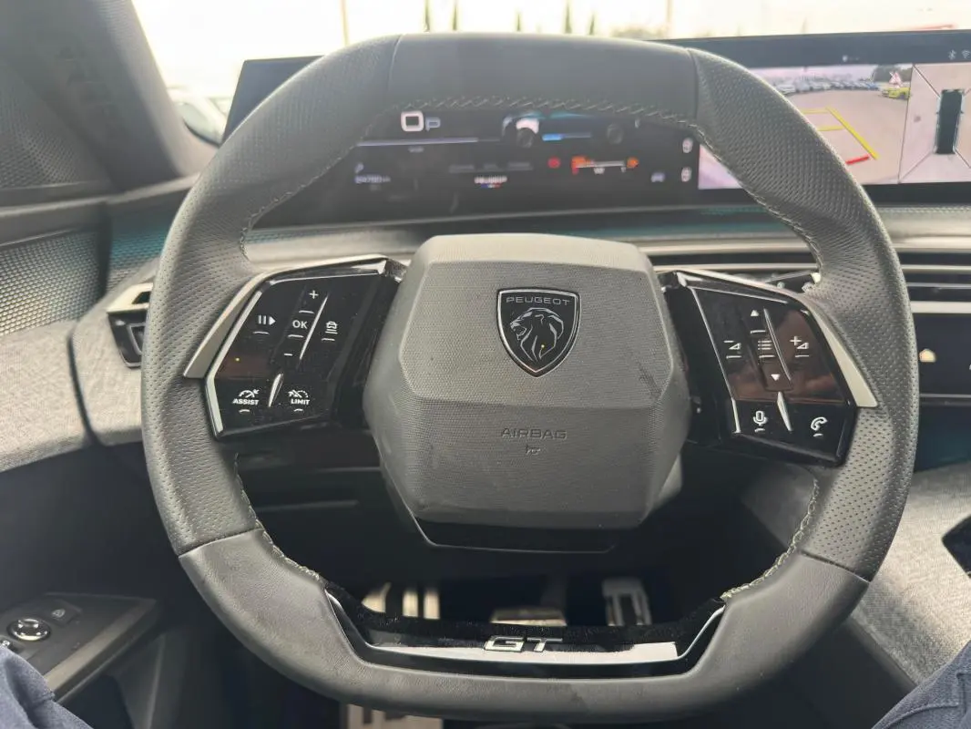 Vue rapprochée du volant noir du Peugeot 5008 Hybrid GT 2025 avec commandes intégrées et tableau de bord numérique.