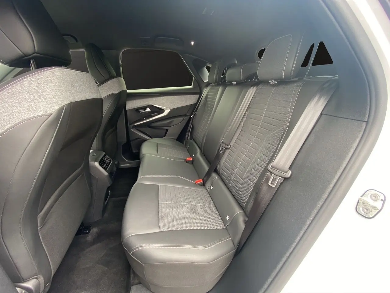 Intérieur arrière du Peugeot 3008 blanc Okenite, vue côté droit montrant les sièges en tissu noir et gris avec ceintures.