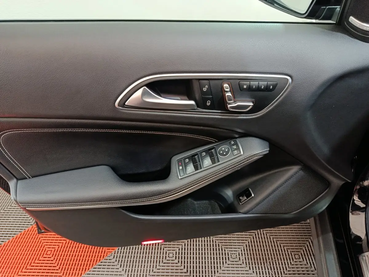 Vue rapprochée de la porte côté conducteur noire du Mercedes GLA 220 d avec commandes électriques et surpiqûres blanches.