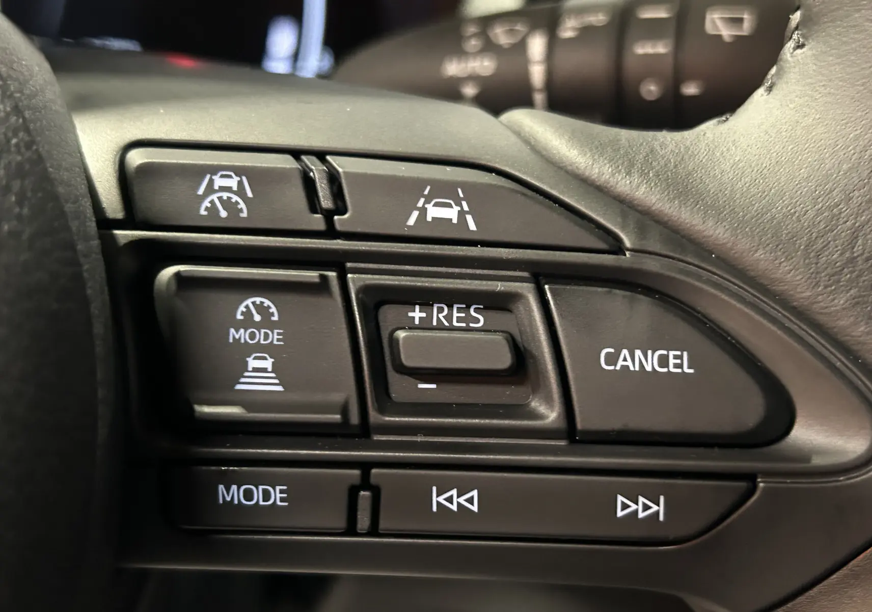 Gros plan sur les commandes au volant noir du Toyota Yaris Cross 130 Design 2025, boutons de régulateur et multimédia visibles.