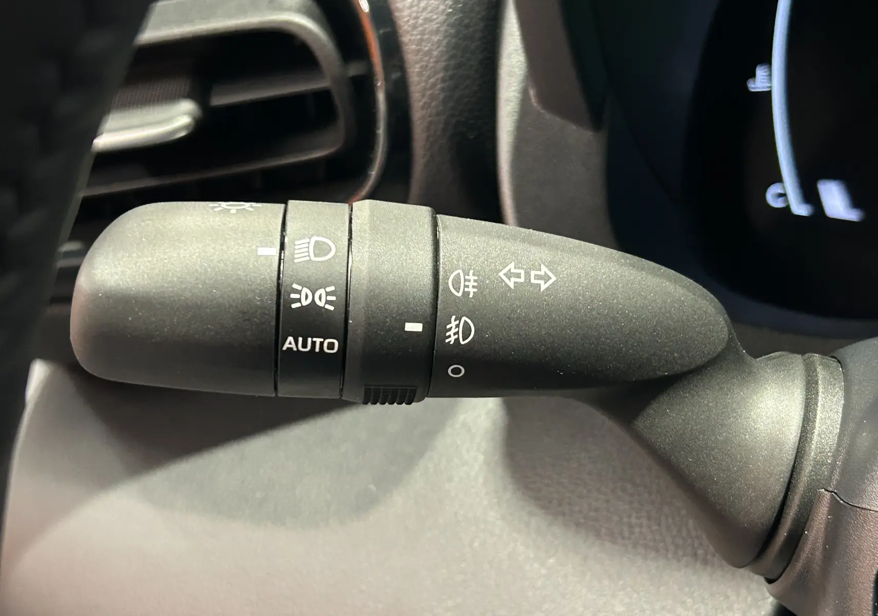 Gros plan sur la commande de feux noire à gauche du volant dans l'habitacle du Toyota Yaris Cross blanc 2025.