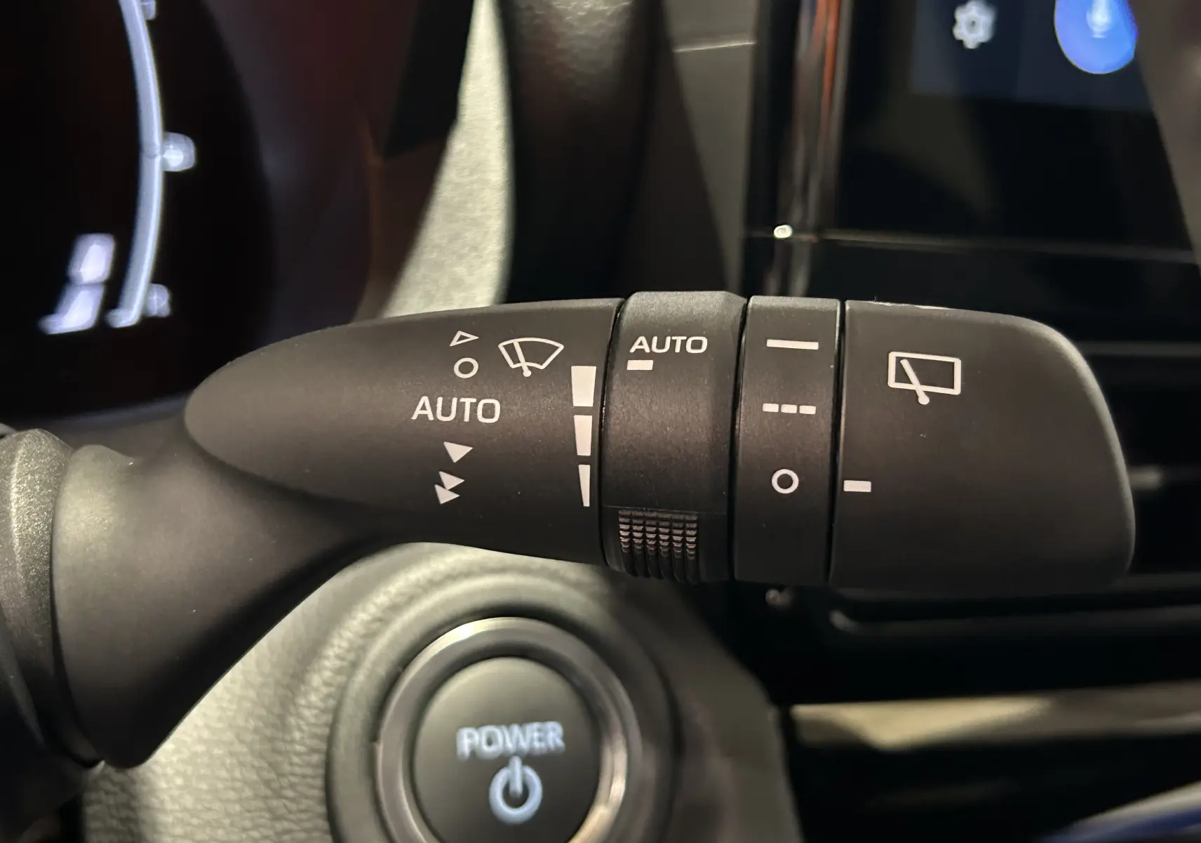 Gros plan sur la commande d’essuie-glace automatique et bouton Power du tableau de bord d’une Toyota Yaris Cross blanche 2025.