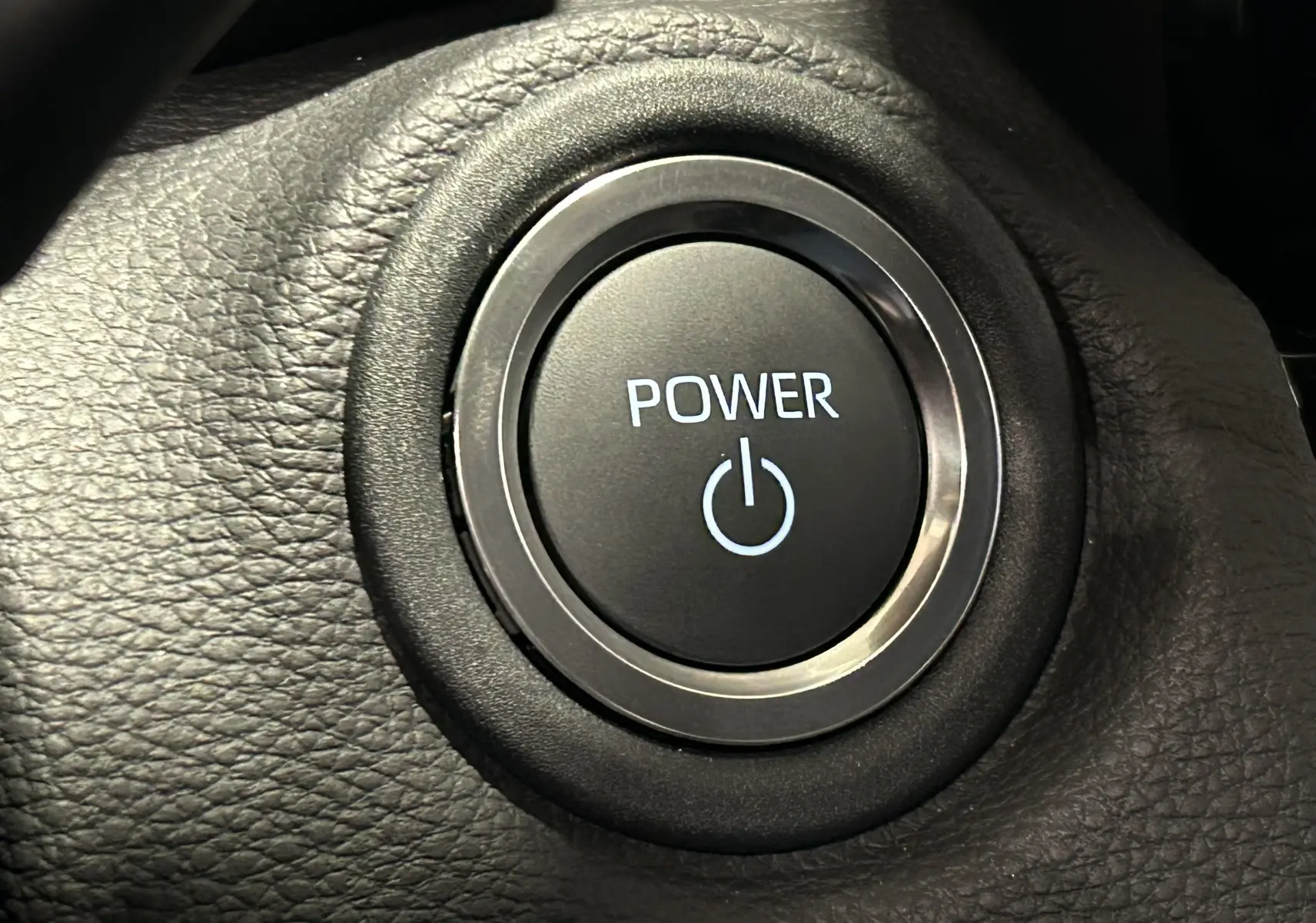 Bouton de démarrage Power en gros plan sur le tableau de bord noir de la Toyota Yaris Cross blanche hybride 2025.