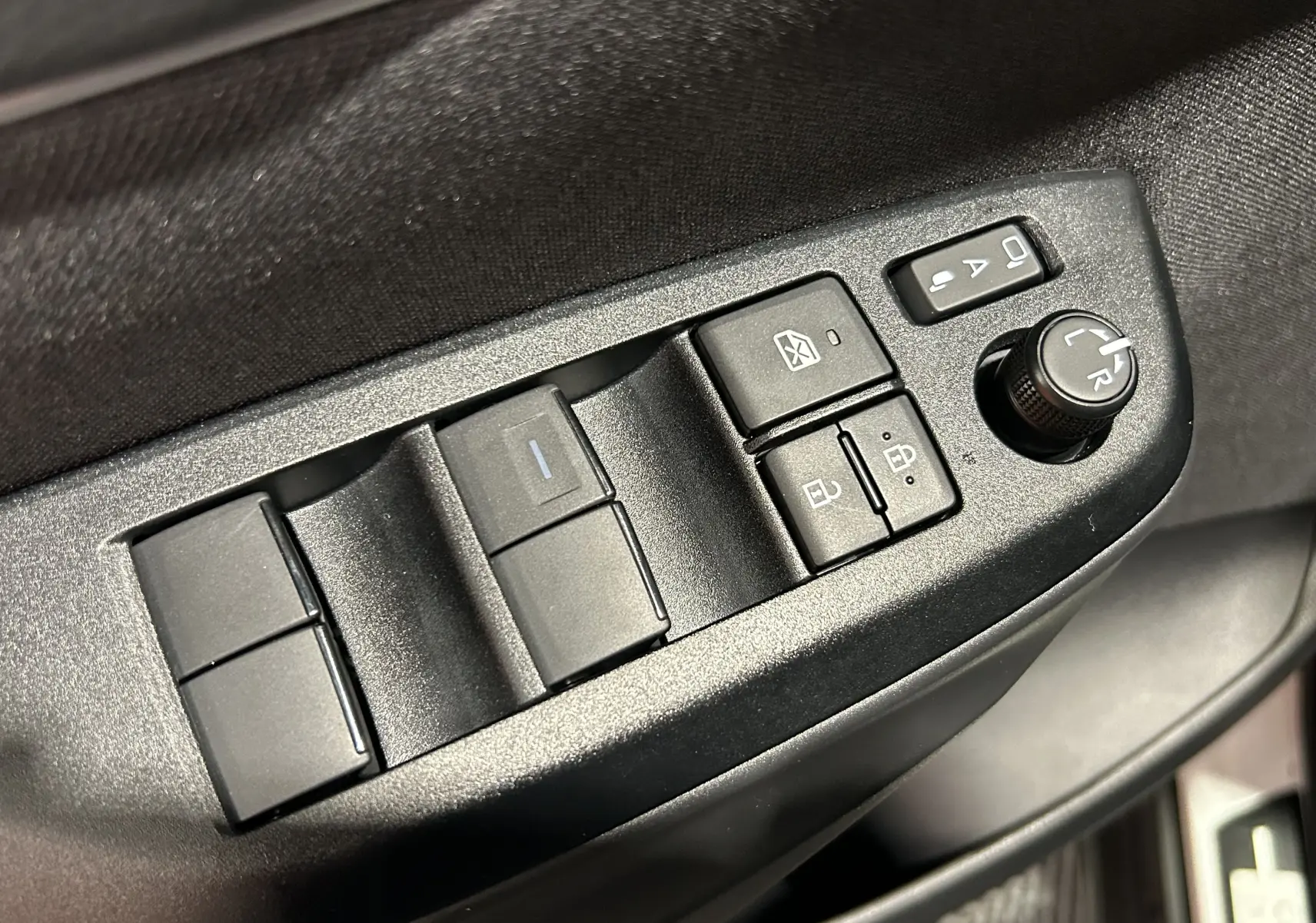 Gros plan sur les commandes des vitres et rétroviseurs côté gauche de la porte d’une Toyota Yaris Cross blanche 2025.