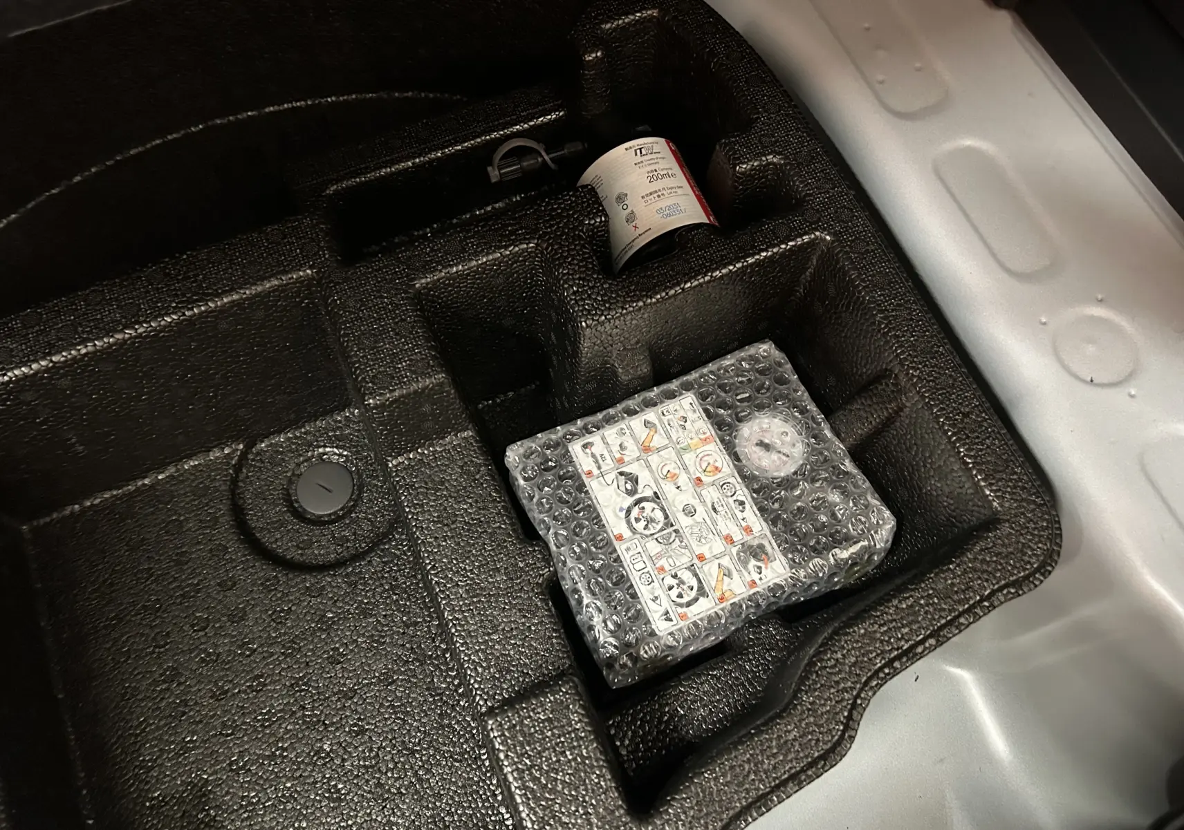 Gros plan sur le compartiment de rangement sous le plancher de coffre de la Toyota Yaris Cross blanche 2025, avec kit de réparation pneus.
