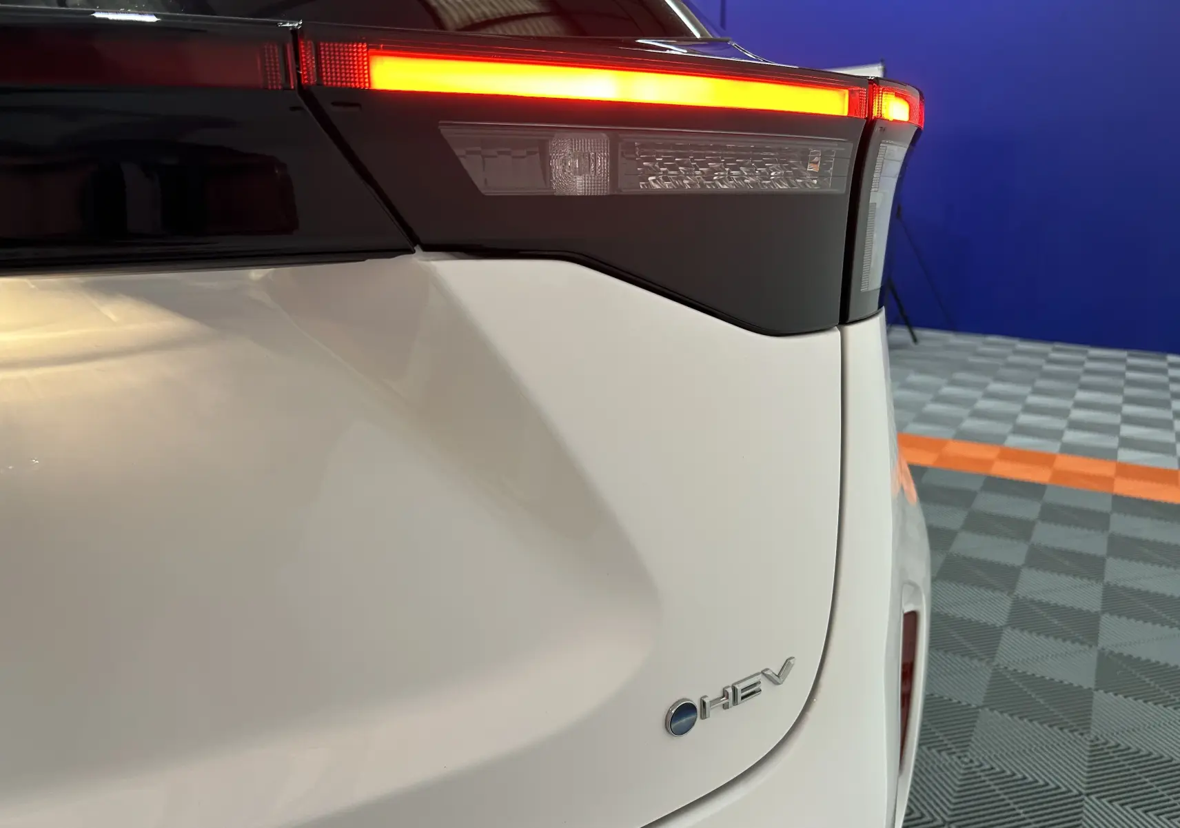 Gros plan sur le feu arrière droit allumé d'une Toyota Yaris Cross blanche hybride avec logo HEV visible.