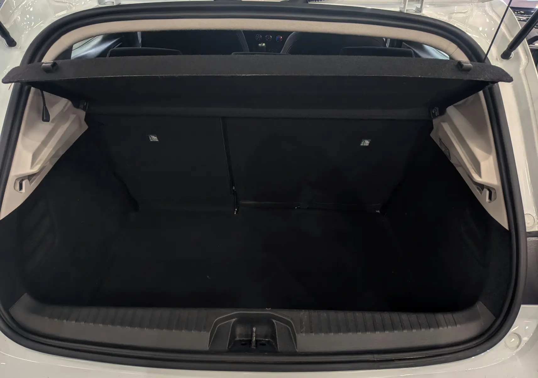 Coffre ouvert vu de l'arrière d'une Renault Clio V Blanc Glacier, montrant l'espace de chargement vide et la plage arrière.