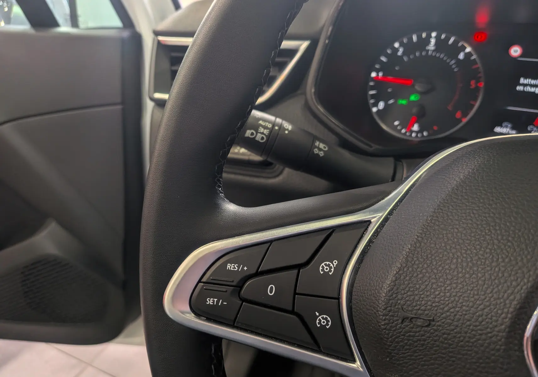 Gros plan sur le volant noir de la Renault Clio V Blue dCi 100 CH BUSINESS avec commandes de régulateur de vitesse visibles.