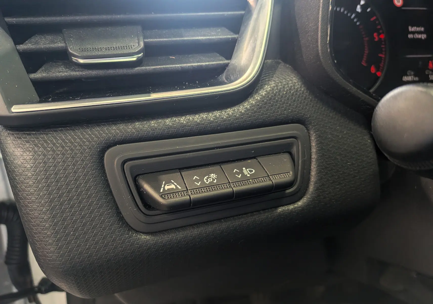 Gros plan sur les commandes d'assistance et réglage des phares dans l'habitacle d'une Renault Clio V blanche.