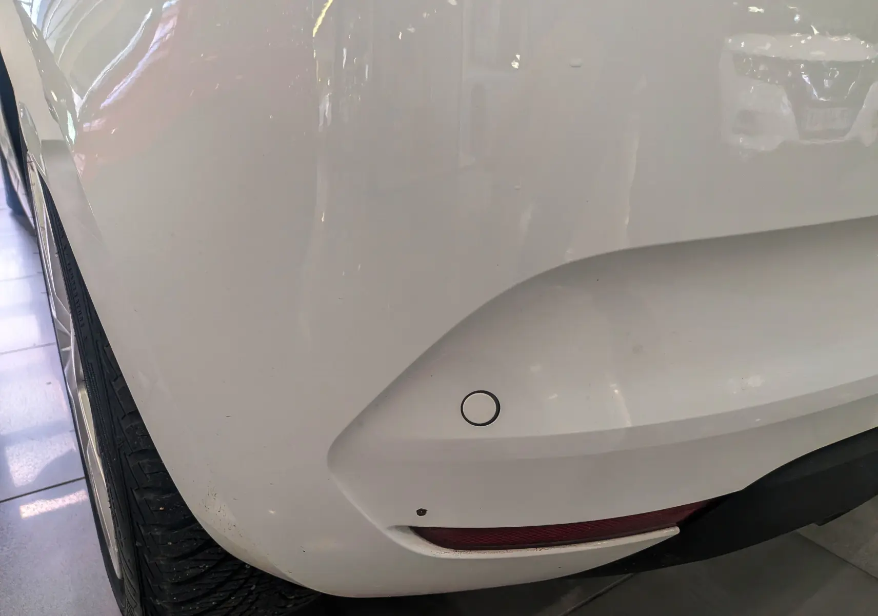 Gros plan sur l'angle arrière gauche blanc glacier d'une Renault Clio V Blue dCi 100 CH BUSINESS avec capteur de recul visible.