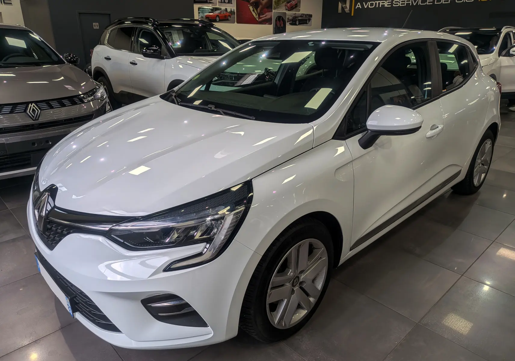 Renault Clio V Blue dCi 100 Business blanc glacier vue 3/4 avant droit en showroom avec jantes alliage.