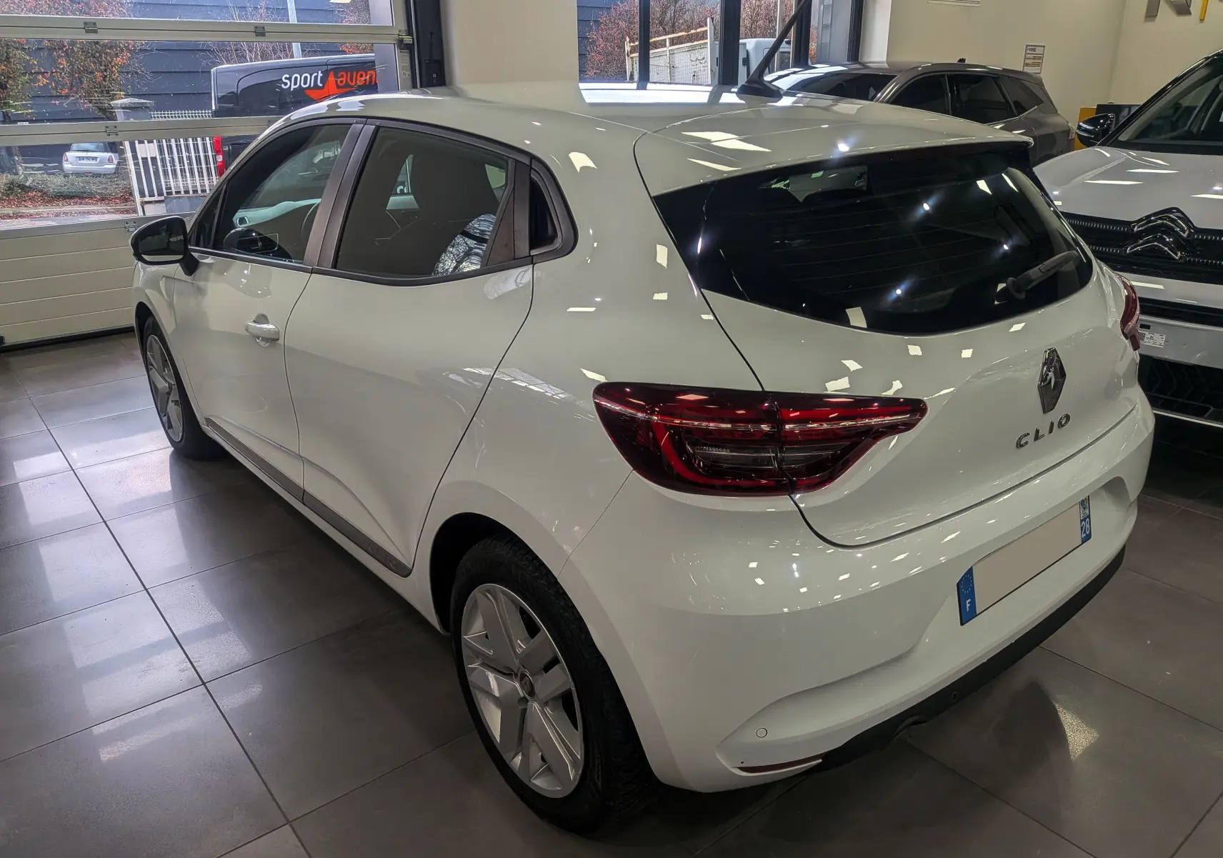 Vue 3/4 arrière droite d'une Renault Clio V Business blanche Glacier en intérieur, avec feux arrière LED distinctifs.