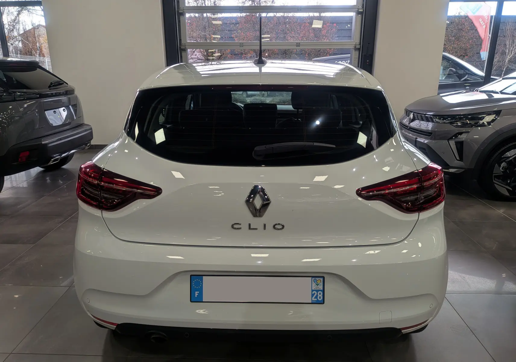 Vue arrière d'une Renault Clio V Blanc Glacier, mettant en valeur ses feux arrière LED et son logo central chromé.