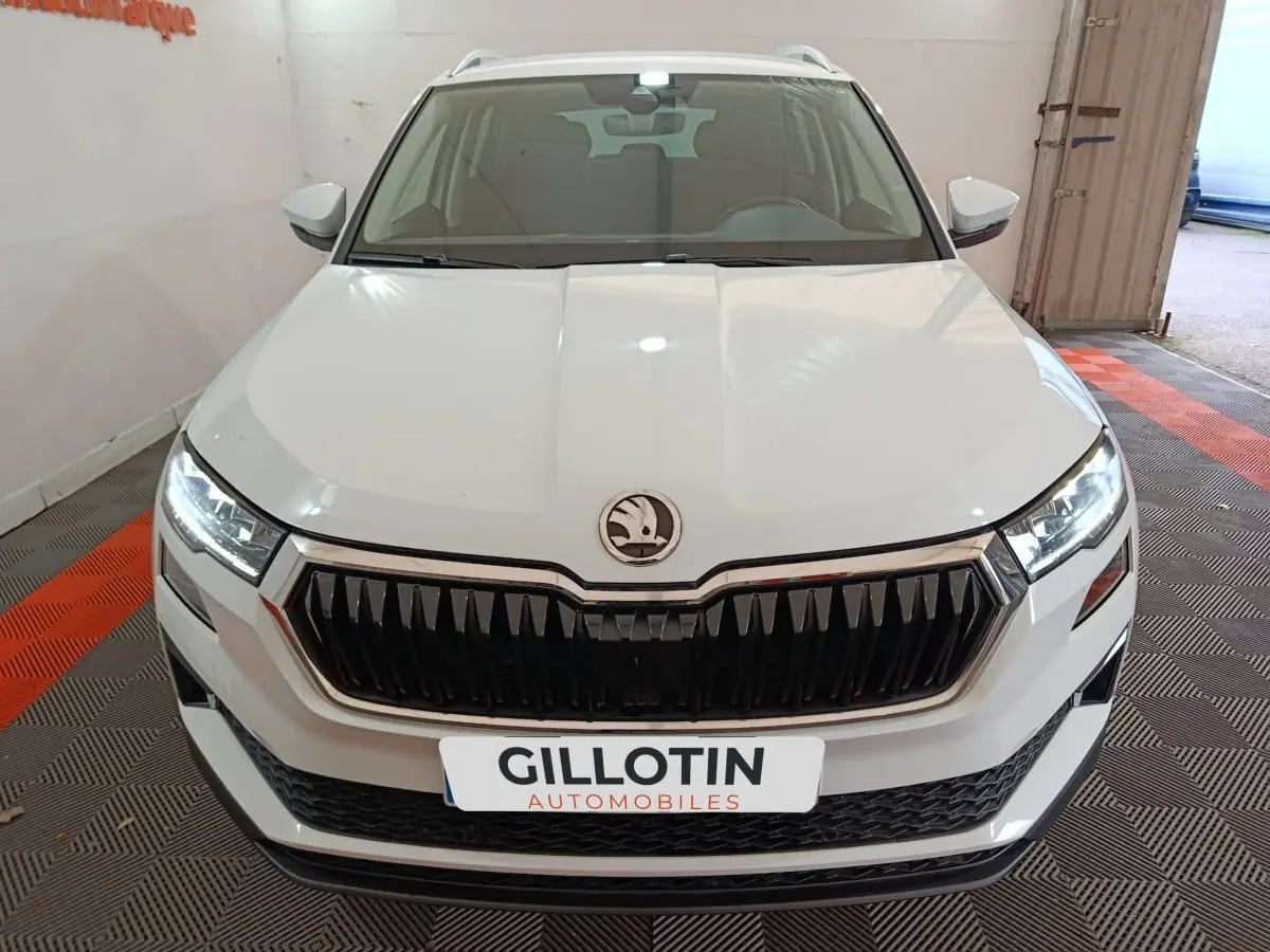 Vue avant d'un Skoda Karoq blanc avec calandre noire et phares LED allumés en intérieur showroom.