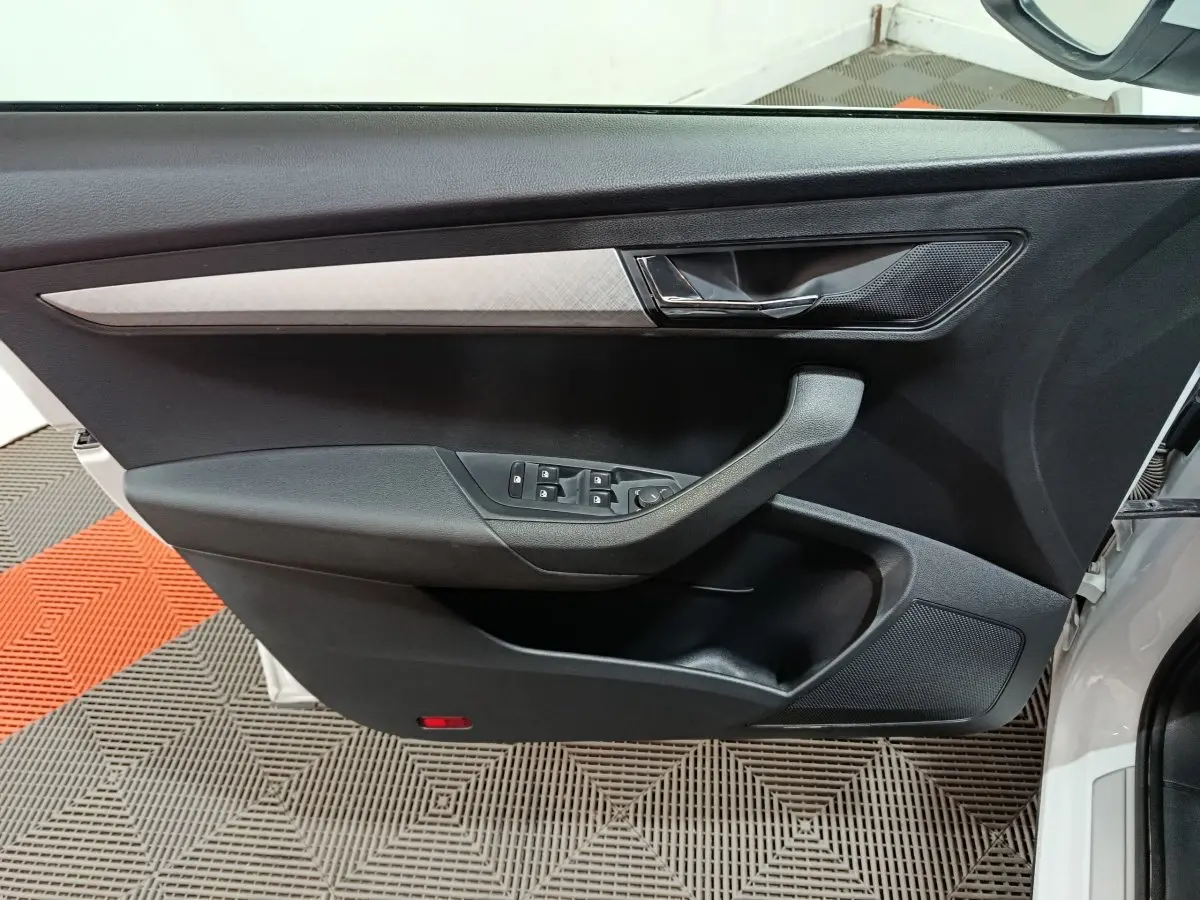 Gros plan sur la porte avant gauche noire du Skoda Karoq 2024 avec commande des vitres et poignée intégrée.