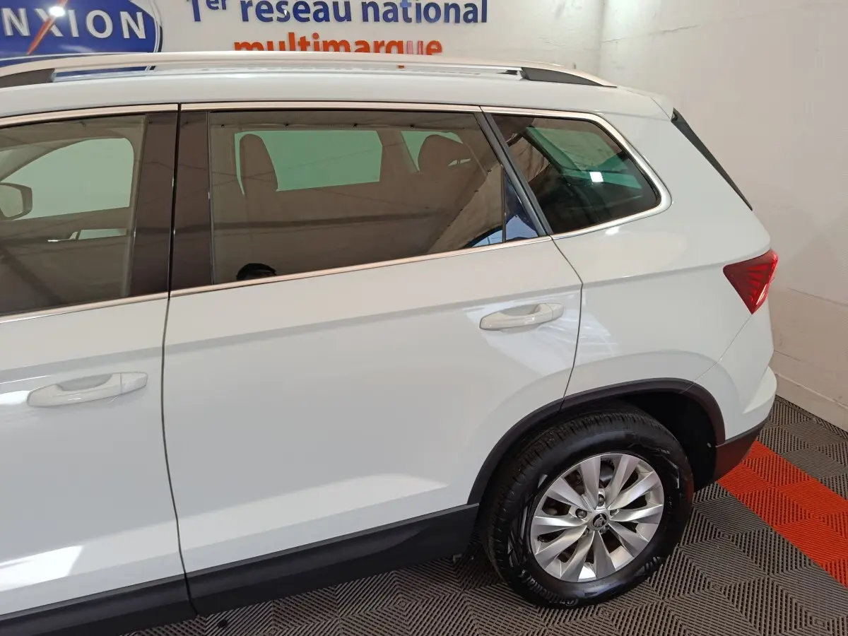 Vue latérale droite d'un Skoda Karoq blanc avec jantes alliage et vitres teintées en intérieur showroom.