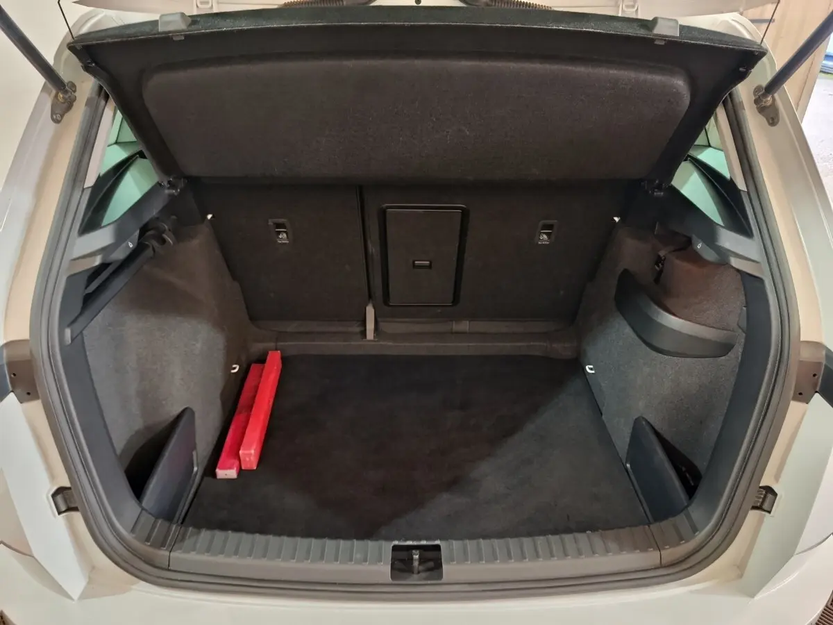 Coffre ouvert vu de l'arrière d'un Skoda Karoq 2024 beige, avec tapis noir et deux objets rouges à gauche.