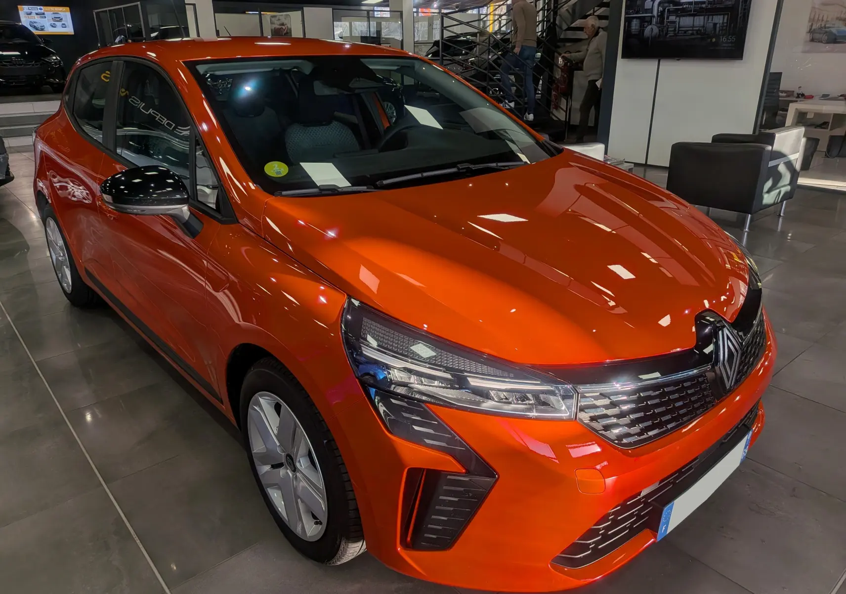 Renault Clio V Orange Valencia vue 3/4 avant droit en intérieur, avec calandre et phares LED distinctifs.