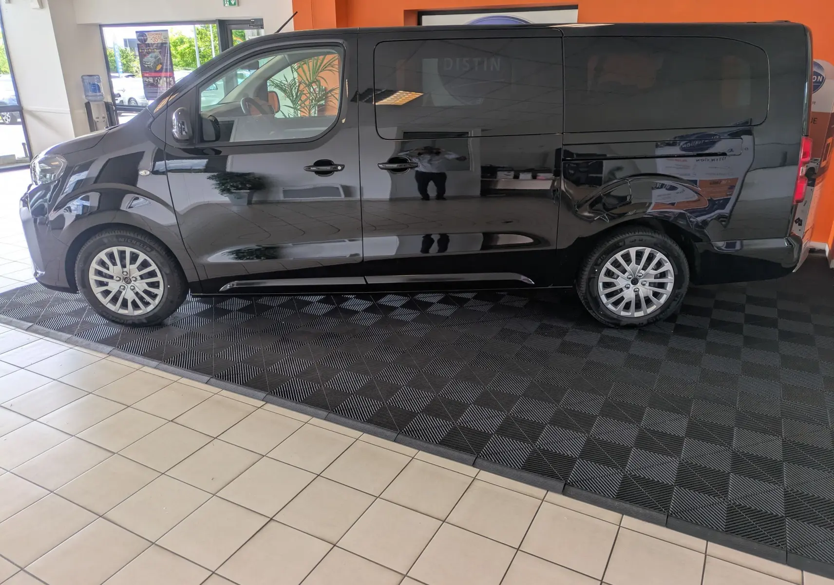 Vue de profil côté gauche d’un Peugeot Traveller noir 2026 en intérieur, avec jantes alliage et vitres teintées.