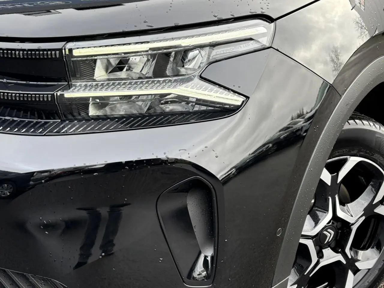 Gros plan sur l’avant droit noir Perla du Citroën C5 Aircross 2025, mettant en valeur le phare LED et la jante alliage 18'' bi-ton.