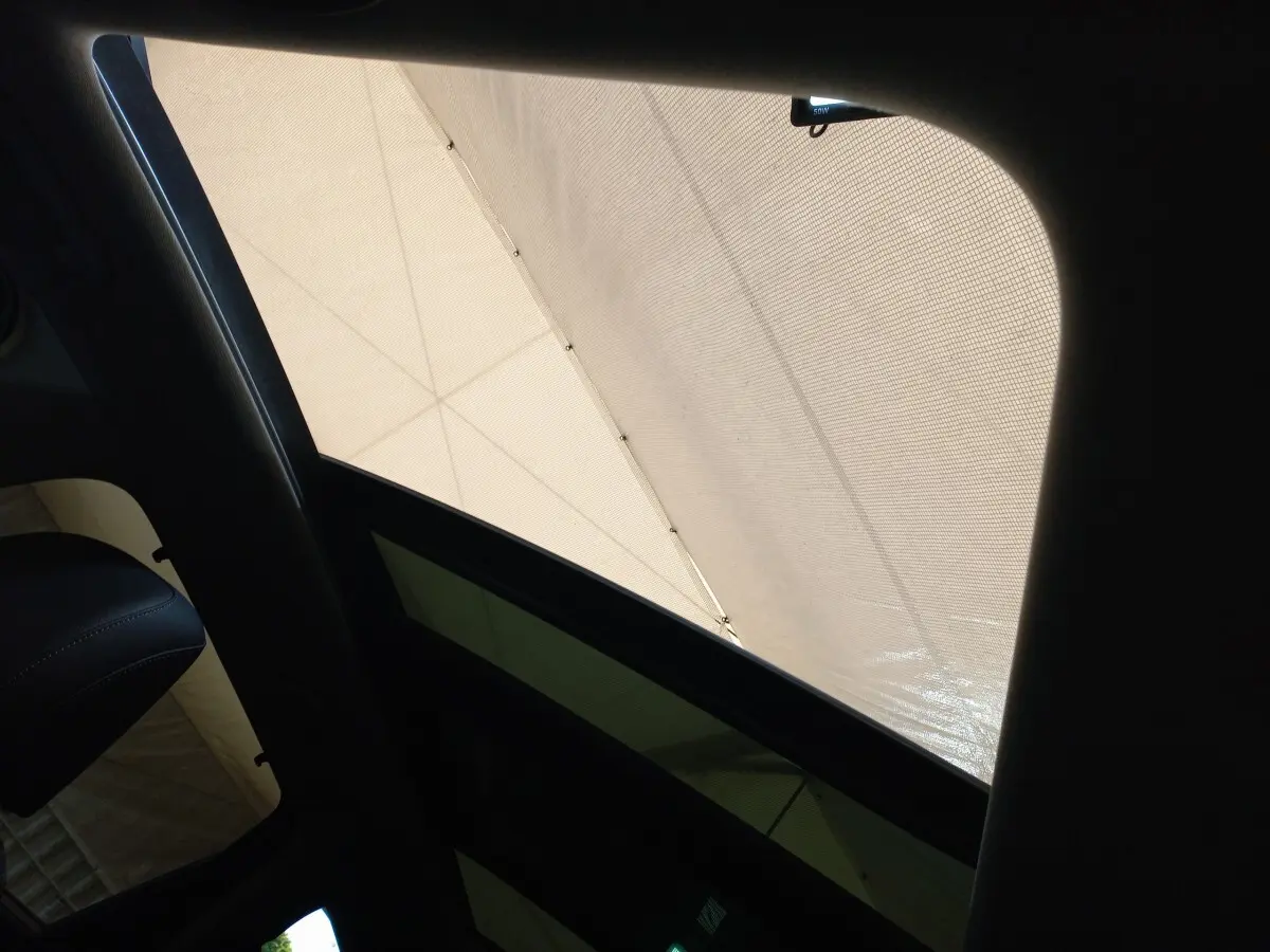 Vue intérieure du toit ouvrant en verre inclinable du Hyundai Santa Fe gris clair, avec pare-soleil déployé.
