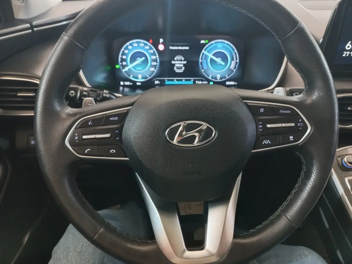 Vue intérieure centrée sur le volant cuir noir et le tableau de bord numérique du Hyundai Santa Fe hybride gris clair 2021.