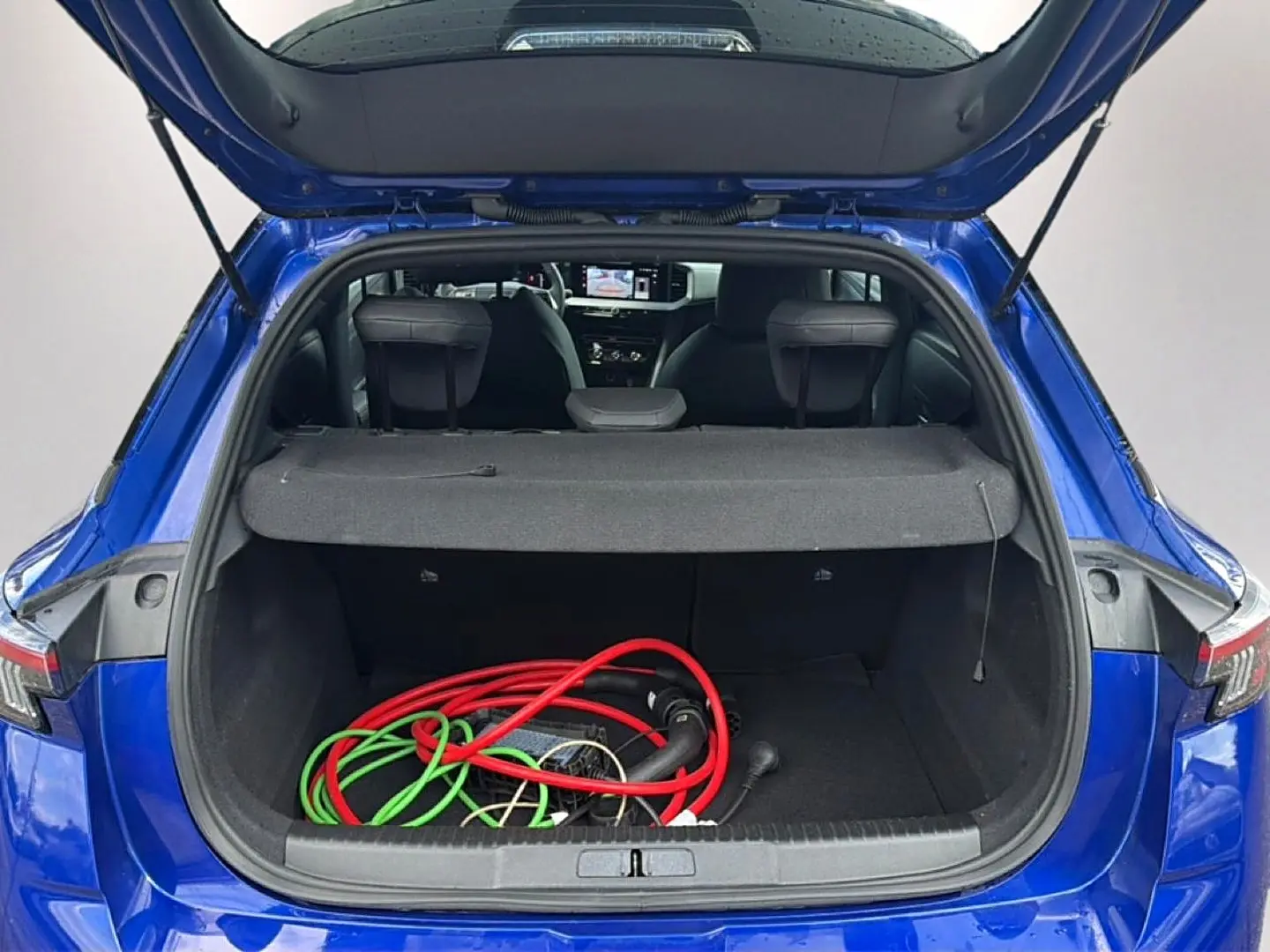 Coffre ouvert vu de l'arrière d'un Opel Mokka Electric 156 gs bleu avec câbles de recharge visibles à l'intérieur.