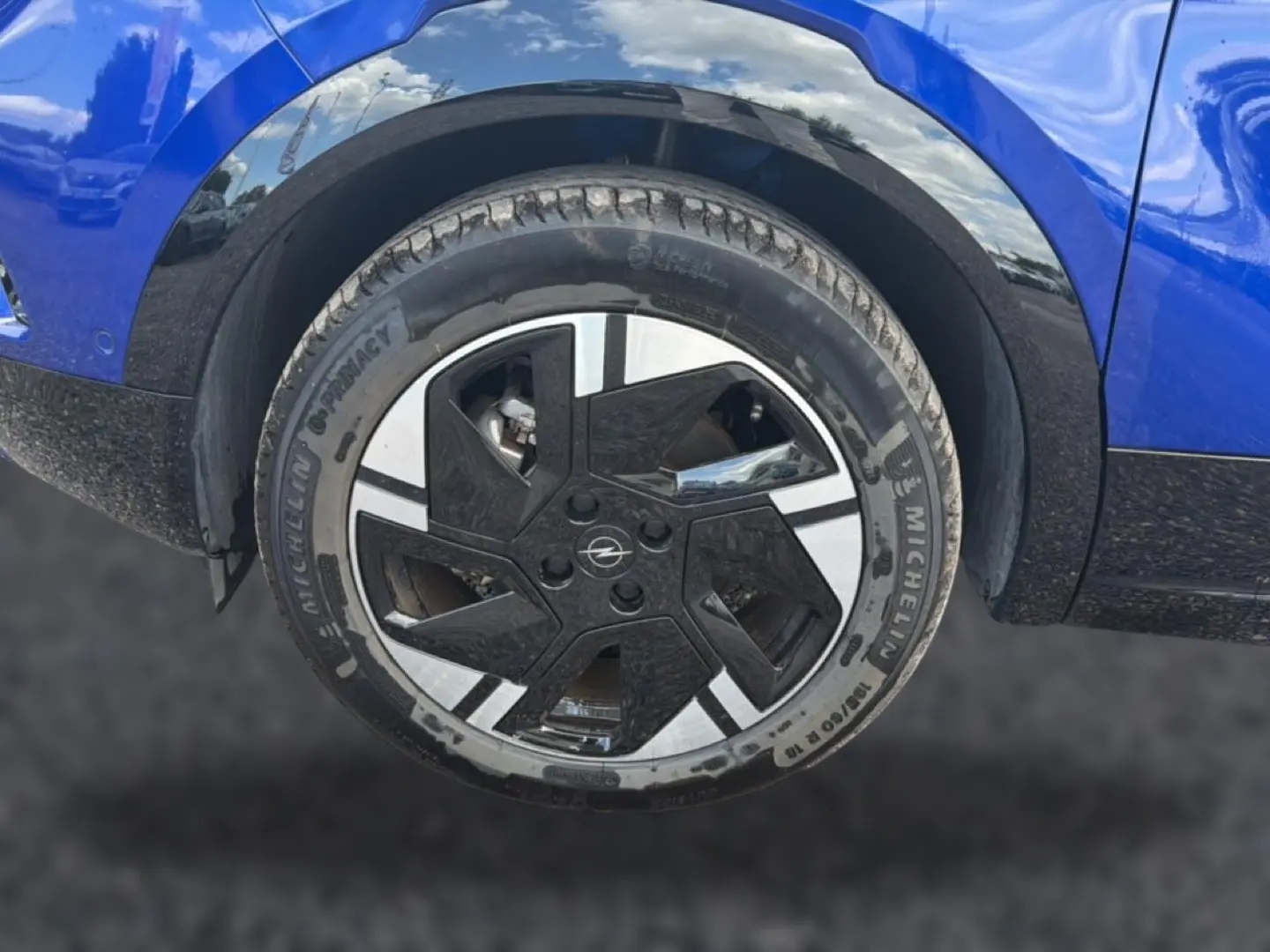 Gros plan sur la roue avant droite d’un Opel Mokka Electric 156 gs bleu, avec jante alu au design moderne bicolore.