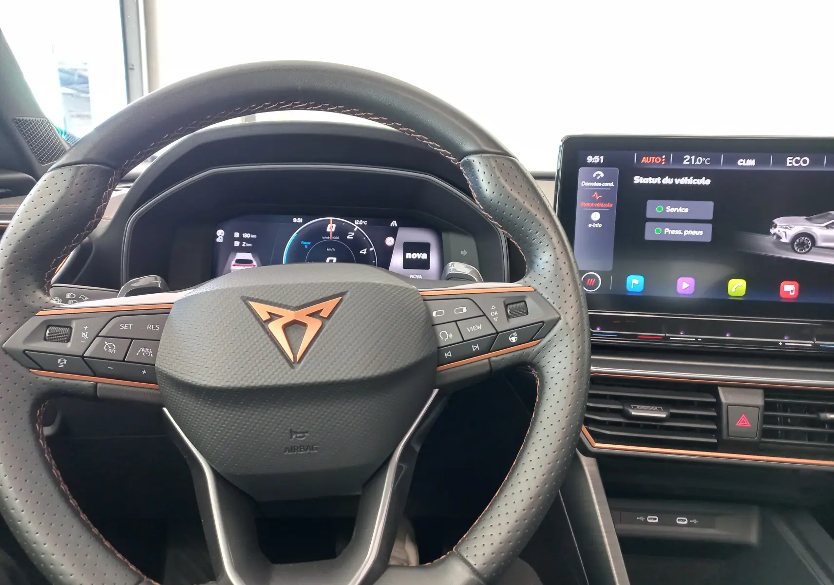 Vue intérieure centrée sur le volant perforé avec logo CUPRA cuivré et écran tactile du tableau de bord.