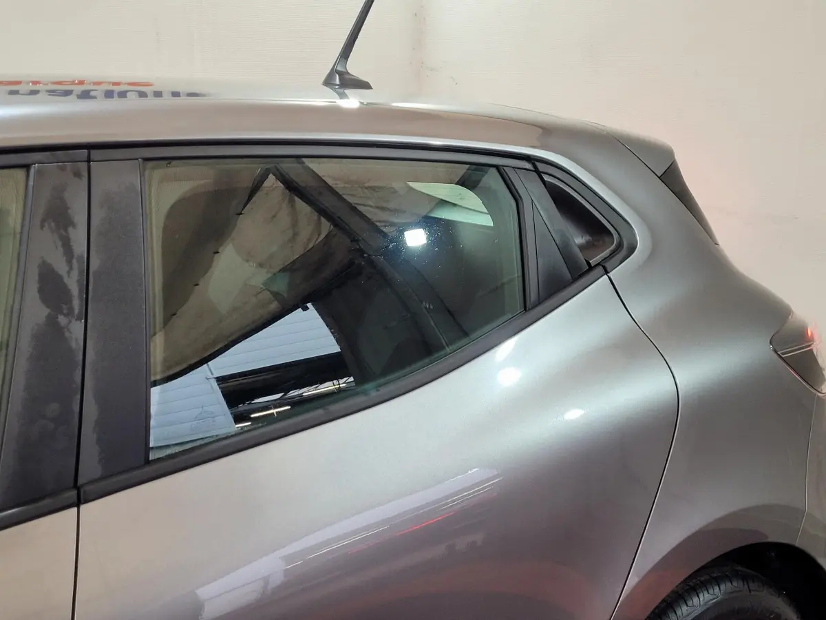 Vue latérale côté droit d'une Renault Clio gris foncé 2025, mettant en valeur la ligne fluide et la vitre arrière teintée.