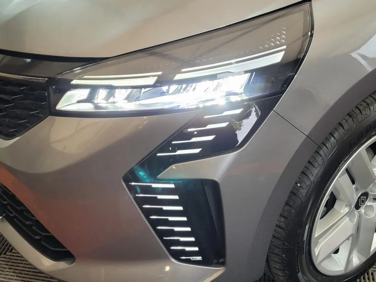 Gros plan sur le phare avant droit allumé d'une Renault Clio gris foncé, avec jante alu visible.