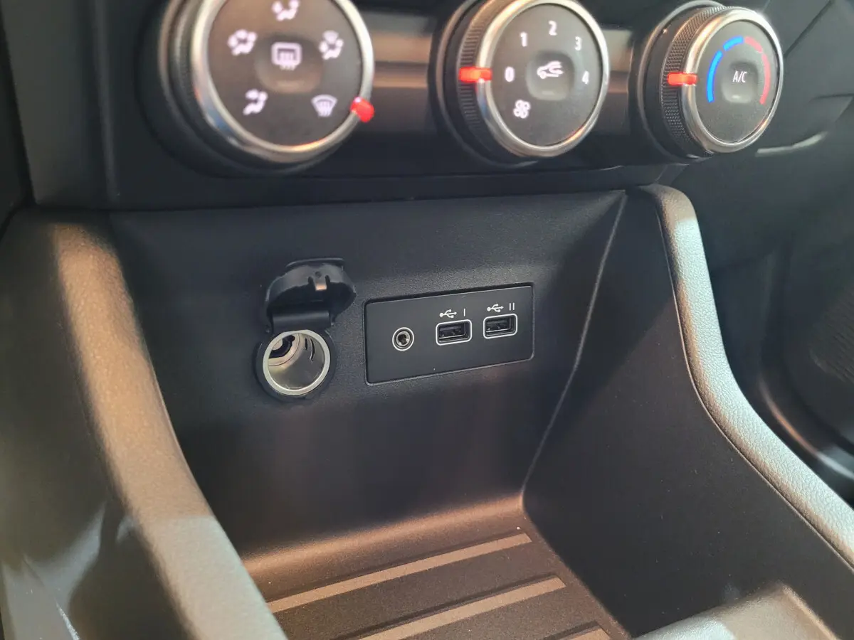Gros plan sur la console centrale noire de la Renault Clio gris foncé, montrant les commandes de climatisation et ports USB.