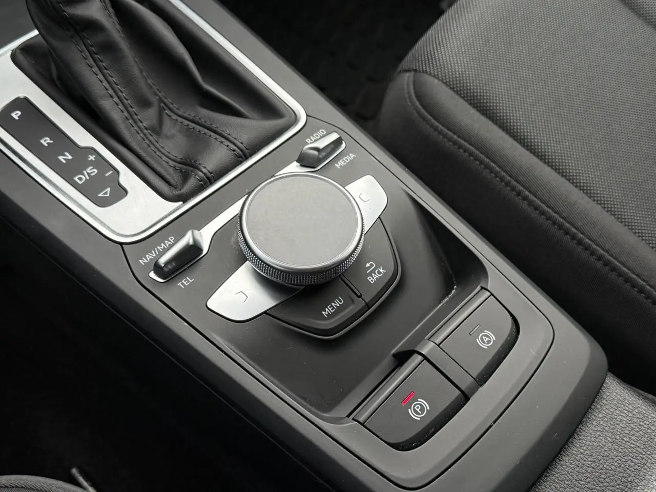 Gros plan sur la console centrale noire de l'Audi Q2 35 TFSI 2023, montrant la molette MMI et le levier de vitesses automatique.