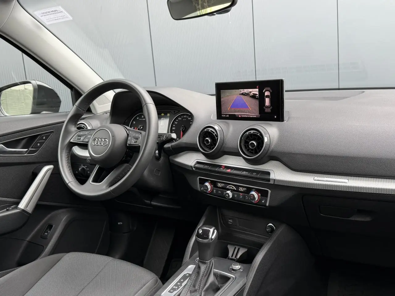 Intérieur Audi Q2 35 TFSI 2023 vu côté conducteur, tableau de bord noir avec écran caméra de recul et climatisation.