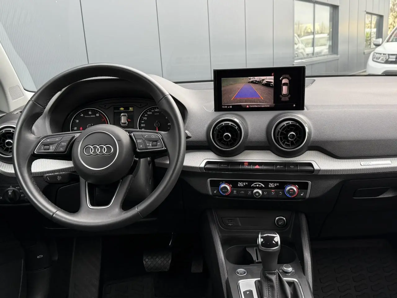 Vue intérieure de l'Audi Q2 35 TFSI S-Line 2023 montrant le volant, l'écran de caméra de recul et la console centrale noire.