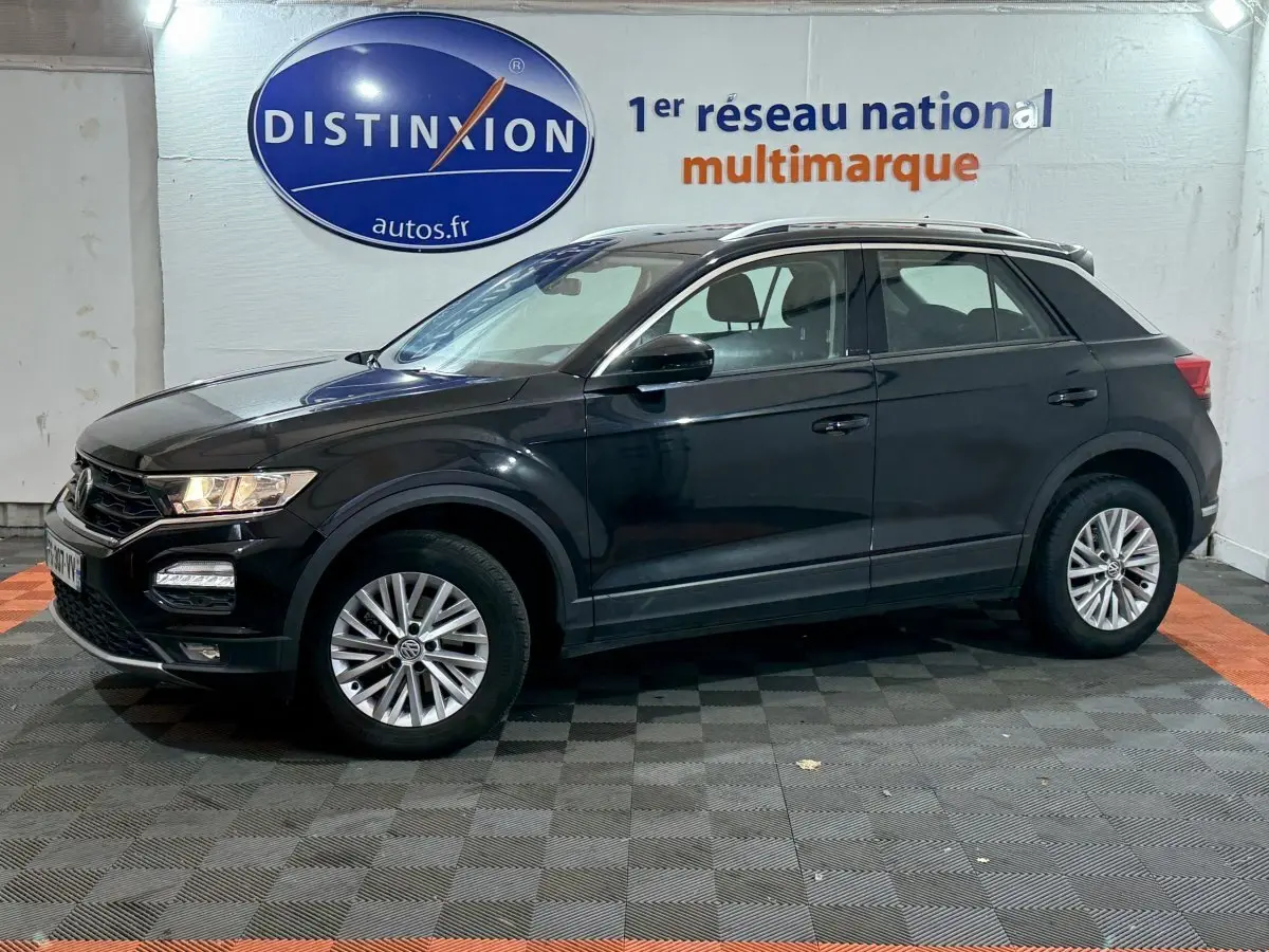 Volkswagen T-Roc noir vue de profil côté gauche dans un showroom avec logo Distinxion en arrière-plan.