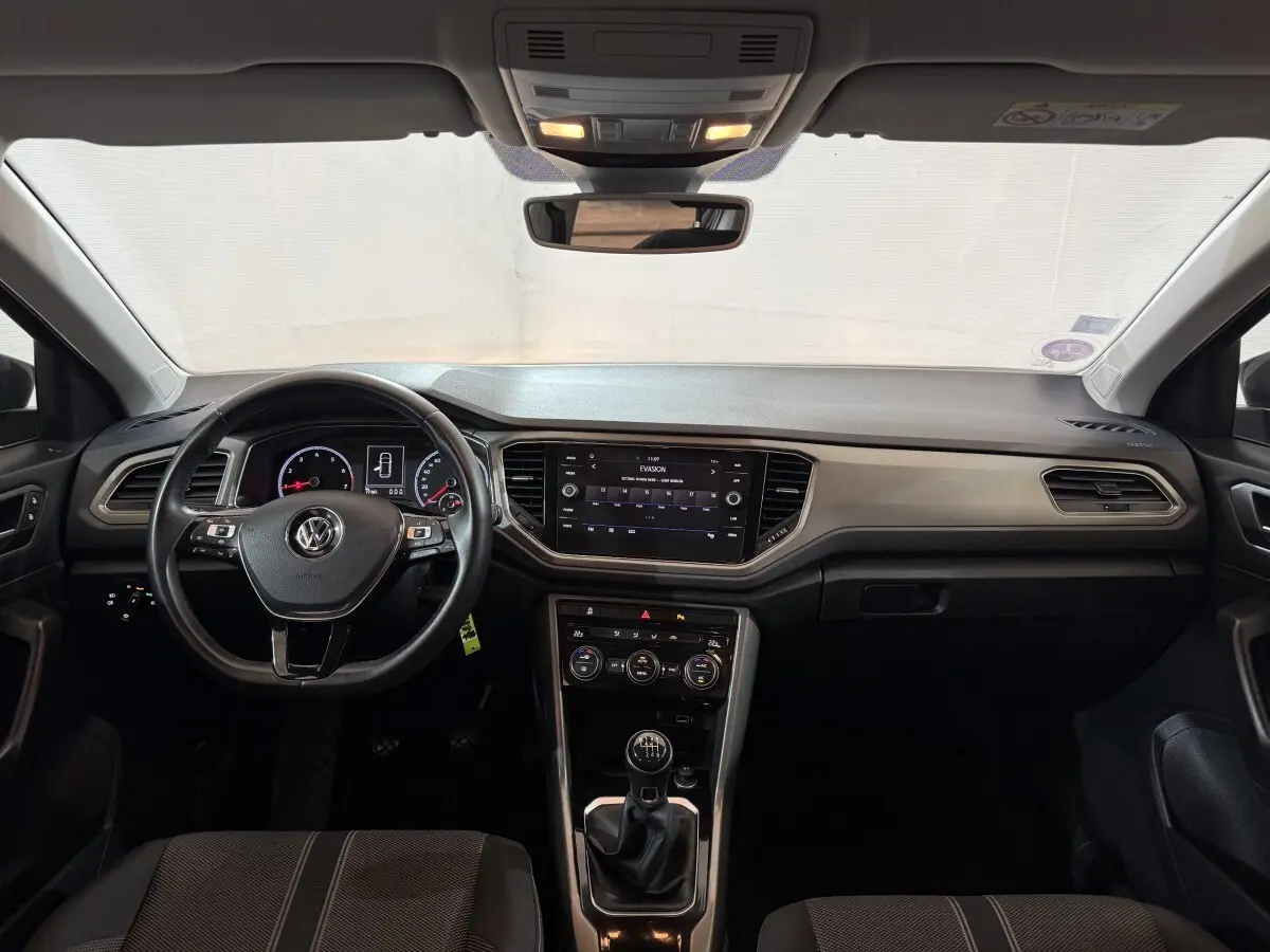 Intérieur avant du Volkswagen T-Roc noir 2020, vue frontale sur tableau de bord, volant cuir et écran tactile central.