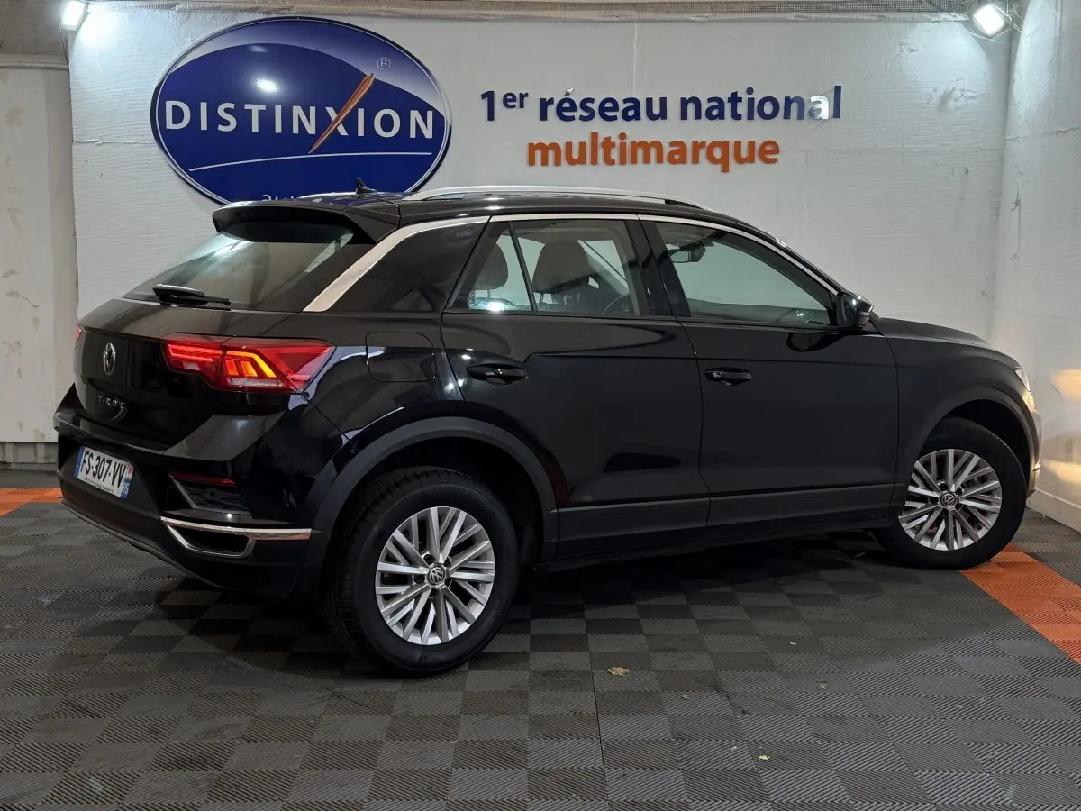 Vue 3/4 arrière côté droit d'un Volkswagen T-Roc noir 2020 dans un showroom avec logo Distinxion en arrière-plan