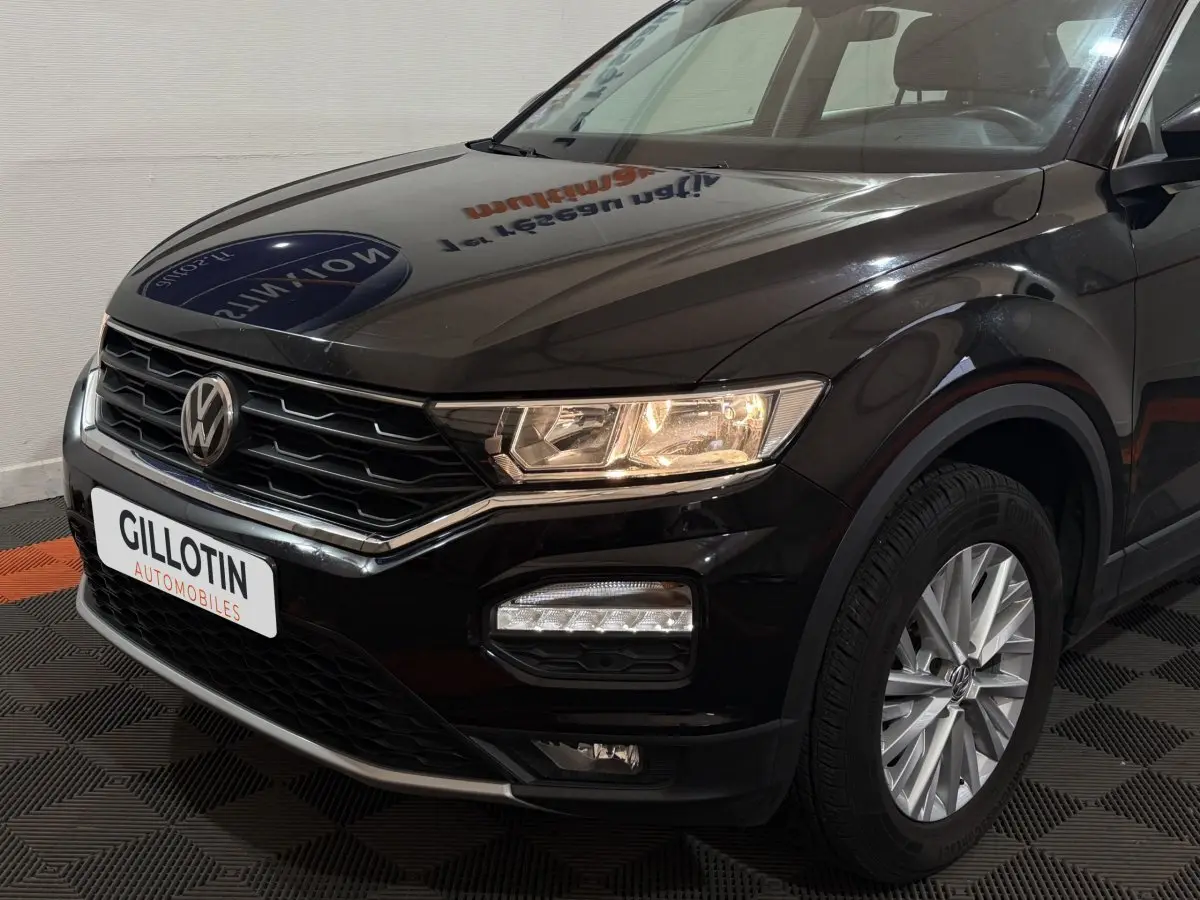 Vue 3/4 avant droit d'un Volkswagen T-Roc noir avec phares allumés et jantes alliage visibles.