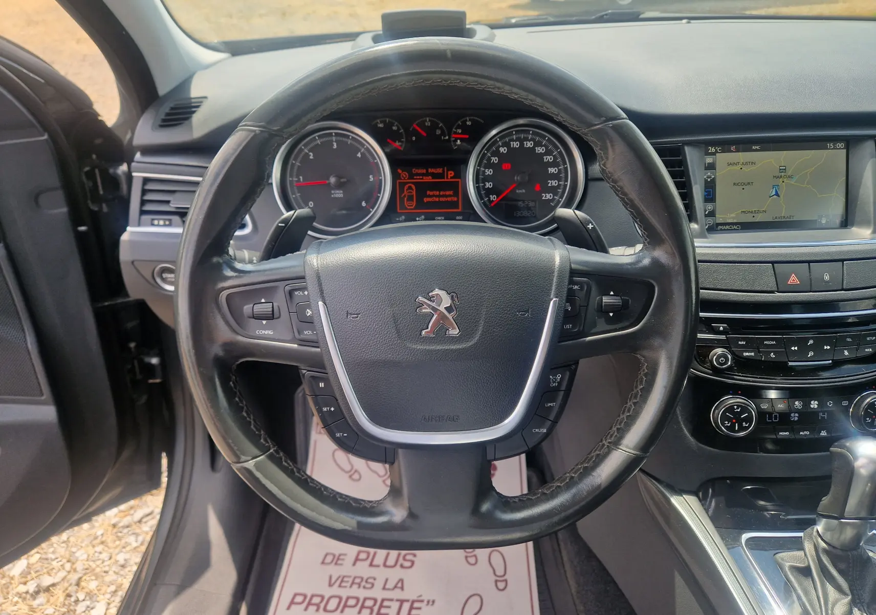 Vue intérieure centrée sur le volant cuir noir du Peugeot 508 SW gris Shark avec tableau de bord et écran GPS visible.