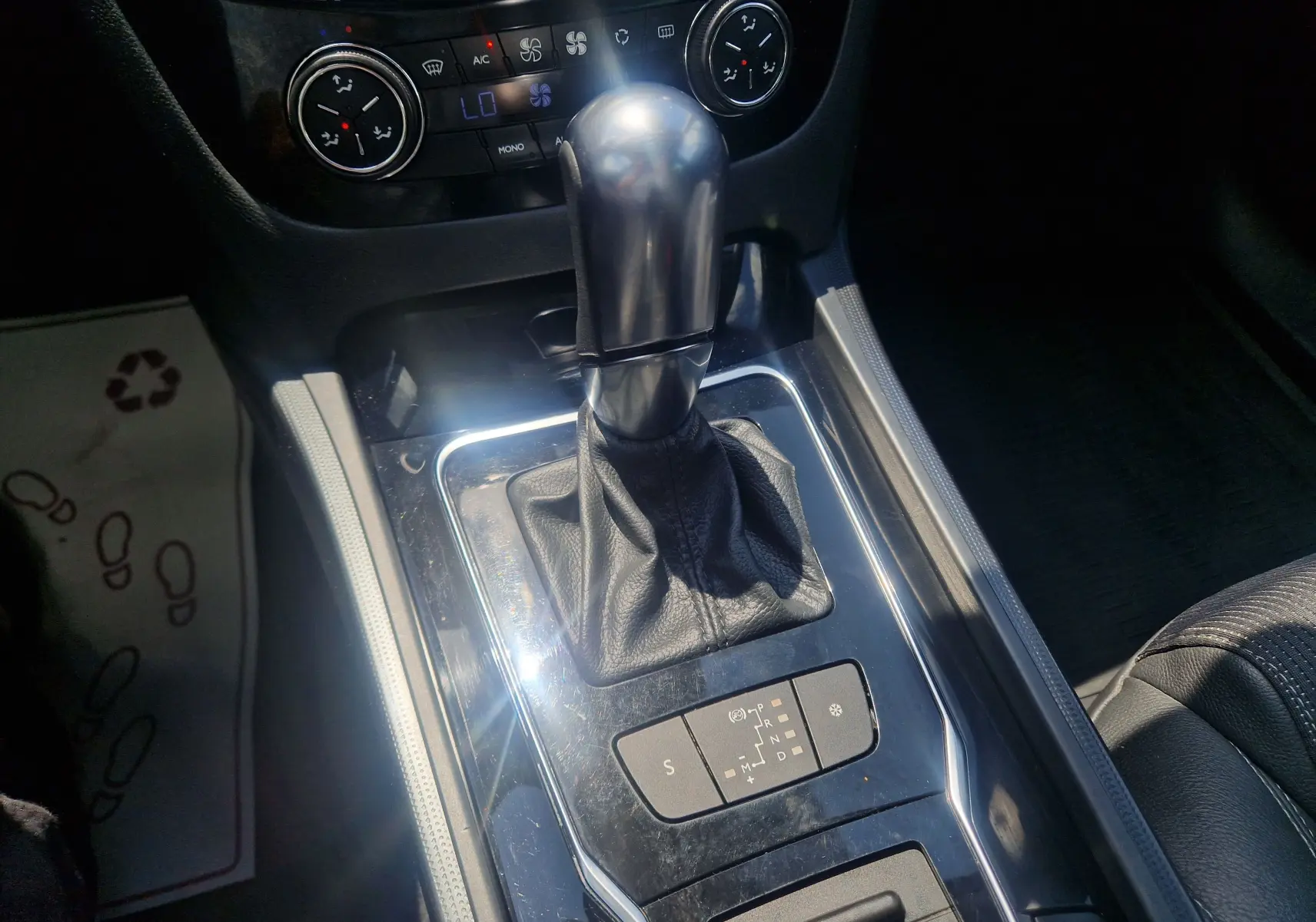 Gros plan sur le levier de vitesse automatique d'une Peugeot 508 SW gris Shark, avec commandes de climatisation visibles en arrière-plan.