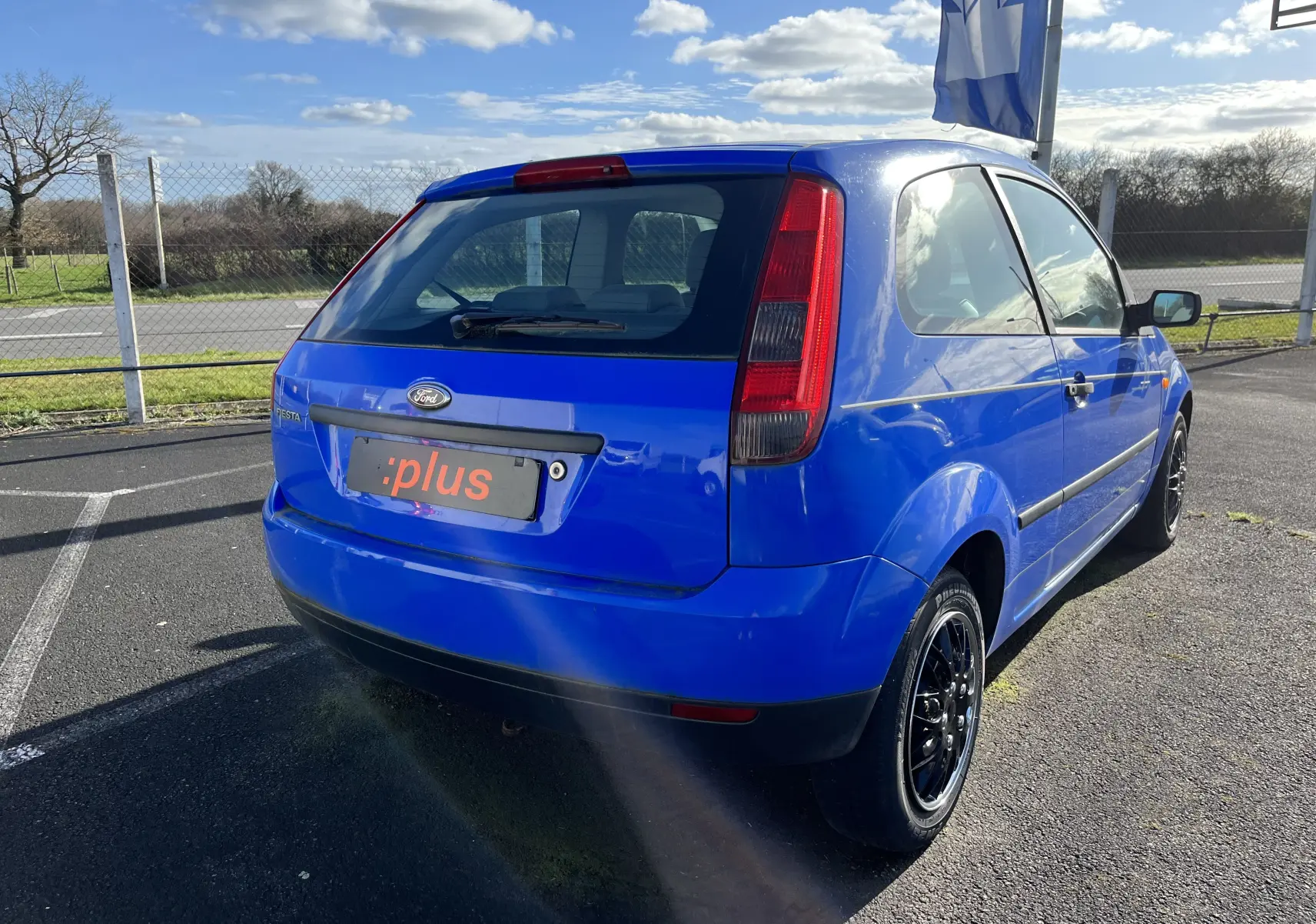 Vue 3/4 arrière droite d'une Ford Fiesta 1.3l essence 3 portes bleu vif avec jantes noires sur parking extérieur.