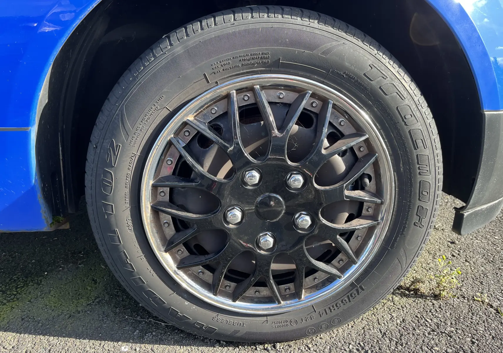 Gros plan sur la roue avant gauche d'une Ford Fiesta bleue de 2003 avec jante noire à multiples branches.