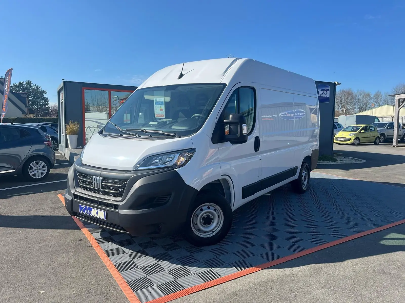 FIAT Ducato Fourgon blanc vu en 3/4 avant droit sur parking, avec calandre noire et jantes acier simples.