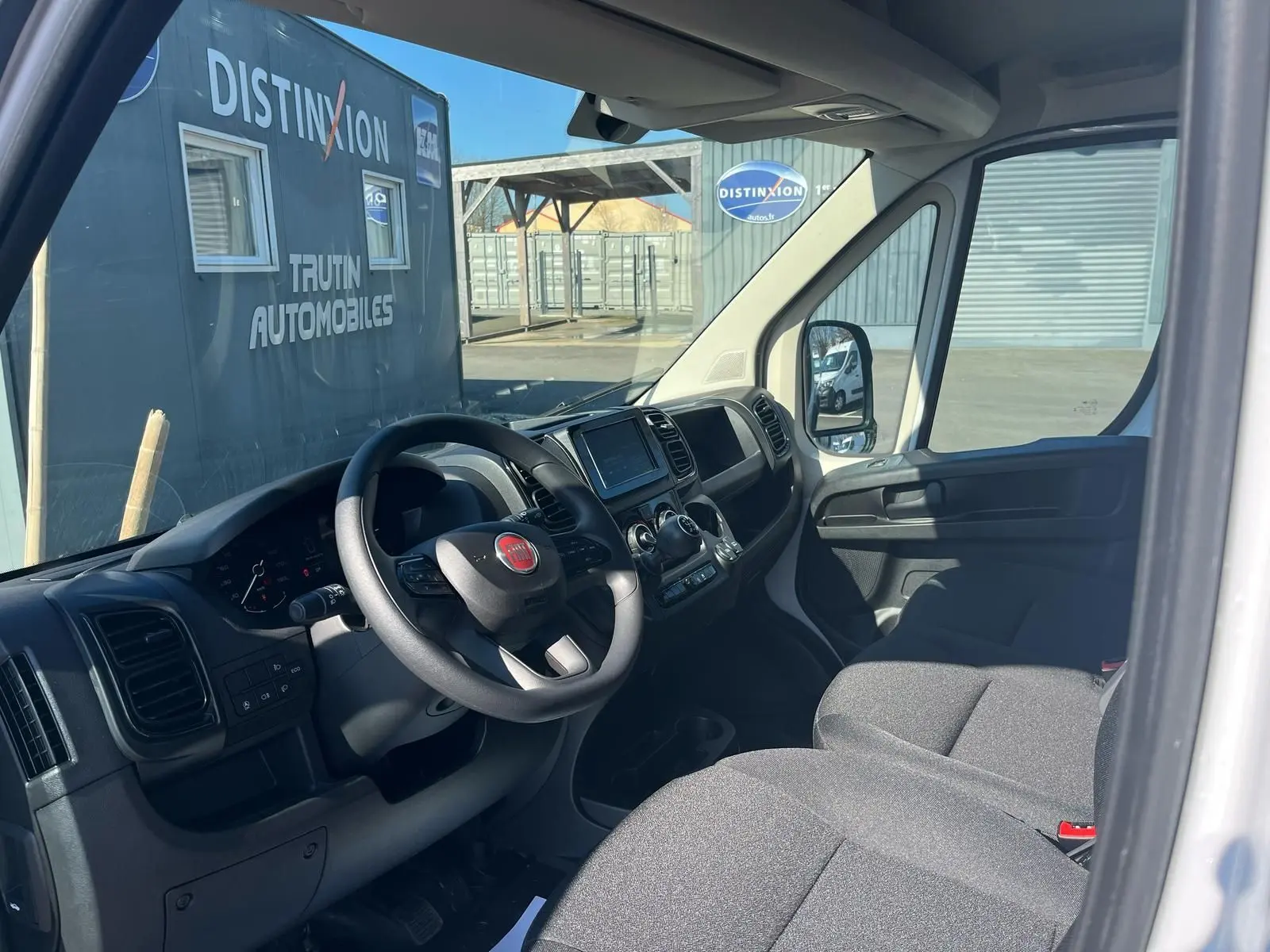 Vue intérieure côté conducteur du Fiat Ducato Fourgon blanc 2023, tableau de bord et sièges gris visibles.
