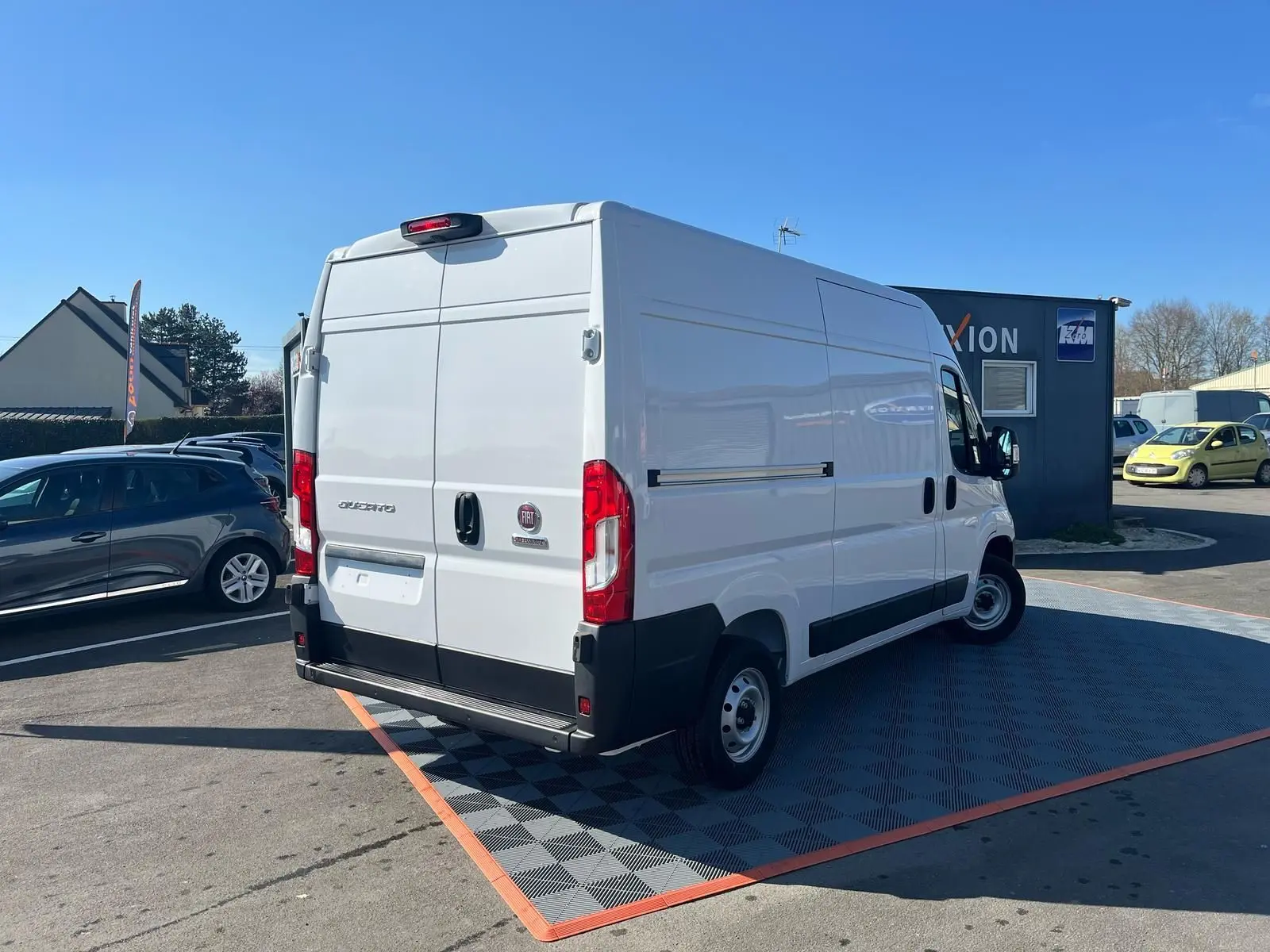 Vue 3/4 arrière droite d'un fourgon blanc FIAT Ducato 2023 avec portes arrière fermées sur parking extérieur.