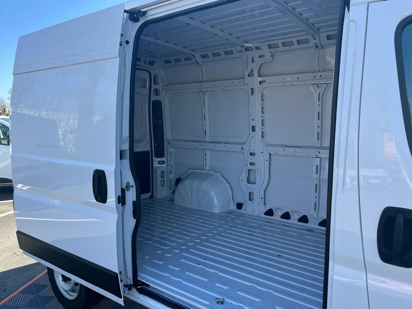 Vue latérale gauche du fourgon blanc FIAT Ducato 2023 avec porte coulissante ouverte montrant l’intérieur vide et métallique.