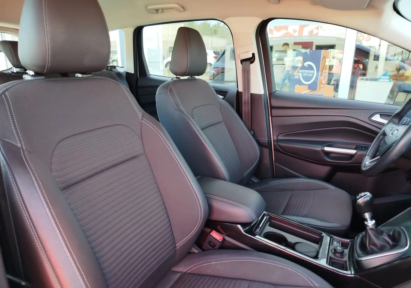 Vue intérieure côté conducteur du Ford Kuga 2019 montrant les sièges tissu gris foncé et la boîte manuelle.